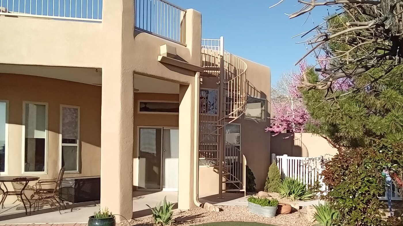 Tan pueblo-style stucco home with a spiral staircase up to a rooftop deck